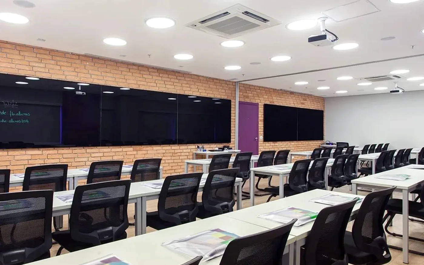 Sala de aula do local, com mesas em fileiras e parede de tijolo aparente